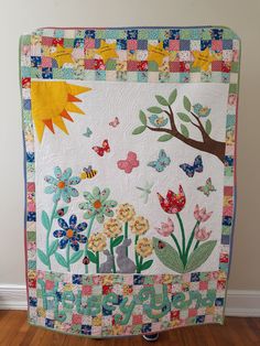 a quilted wall hanging in the corner of a room with flowers and butterflies on it