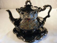 a black and gold tea pot with saucer on it's side sitting on a white surface