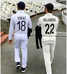 two men in white baseball uniforms walking down the street with their backs to each other