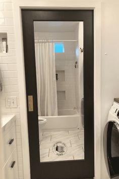 a washer and dryer in a bathroom with white tile flooring next to a black door