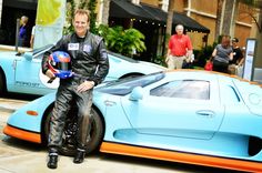 a man sitting on top of a blue sports car next to other cars and people