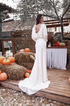 a woman in a white dress standing on a wooden deck next to pumpkins and hay bales