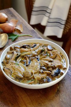 a bowl of mushroom soup sitting on top of a wooden table next to some vegetables