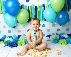 a baby wearing a tie sitting on the floor in front of blue and green balloons