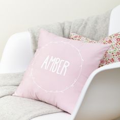 a pink pillow sitting on top of a white chair next to a flowered pillow