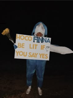 a man dressed as a shark holding a sign that says hoco finna be lit if you say yes