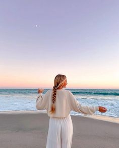 a woman standing on top of a sandy beach next to the ocean with her arms outstretched