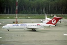 two airplanes are parked on the tarmac at an airport, one is red and white