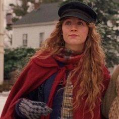 a woman with long hair wearing a red coat and hat standing next to a man