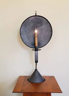 a metal object with a candle on top of it sitting on a wooden table next to a white wall