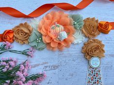 an arrangement of flowers and ribbons on a white wooden table with orange ribbon around it