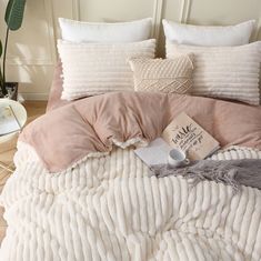 a bed covered in pink and white pillows next to a book on top of it