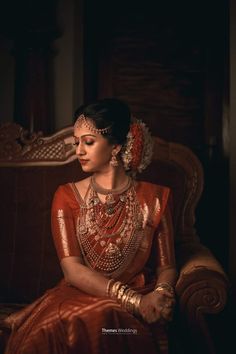 a woman in an orange dress sitting on a chair with her hands clasped to her chest