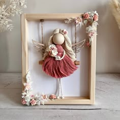 a wooden frame with a doll hanging from it's sides and flowers around the edges