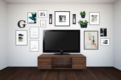 a flat screen tv sitting on top of a wooden cabinet in front of a wall filled with pictures