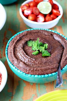 a bowl of chocolate hummus next to bowls of tomatoes and limes on a table