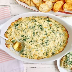 a white dish filled with cheese and spinach dip next to some crackers on the side