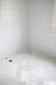 an empty bathroom with white tile on the walls and floor, in front of a window