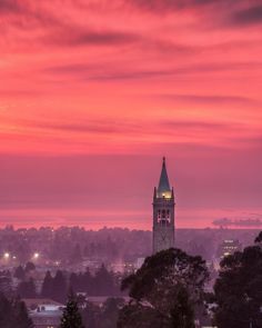 a large clock tower towering over a city under a pink sky at sunset or dawn