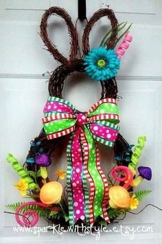 a wreath with flowers and ribbons hanging on the front door, decorated like an easter bunny