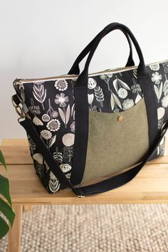 a black and white floral bag sitting on top of a wooden table next to a plant