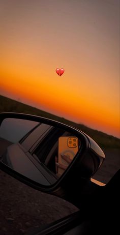 a car's side view mirror with the sun setting in the background