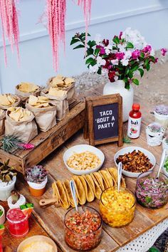 a table filled with food and drinks on top of a wooden tray next to pink flowers