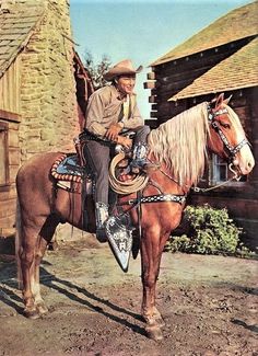 a man riding on the back of a brown horse in front of a stone building