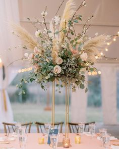 an elegant centerpiece with flowers and feathers sits on a table at a wedding reception