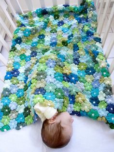 a baby laying on top of a crib next to a green and blue blanket