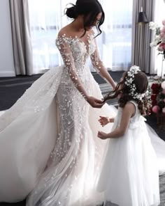 two women in wedding gowns standing next to each other and one is holding the bride's hand