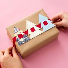 someone is wrapping up a gift on a pink surface with red ribbon and tape around it