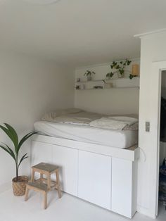 a bed sitting on top of a white shelf next to a potted plant