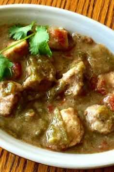 a white bowl filled with meat and vegetables on top of a wooden table next to a spoon