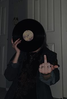 a woman holding up a black record in front of her face and making the peace sign