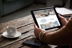 a person sitting at a wooden table with a tablet computer and cup of coffee in front of them