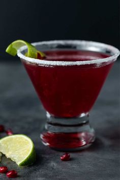 a red cocktail with lime and pomegranate garnish