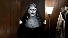 a woman dressed as the nun holding a lamp in front of her face and standing next to a wooden wall