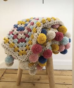 a multicolored crocheted blanket sitting on top of a wooden stool