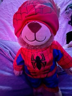 a spiderman teddy bear sitting on top of a purple bed with pink sheets and pillows