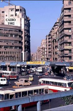 many buses and cars are driving on the street in front of tall buildings with balconies