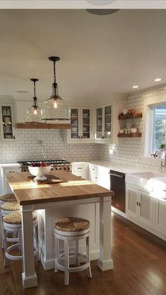 a large kitchen with white cabinets and wooden counter tops, two stools at the island