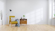 an empty room with a yellow chair and wooden table in front of a white wall