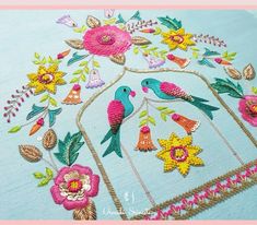 an embroidered piece with birds and flowers on blue fabric, in the shape of a birdcage