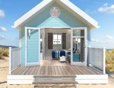 a blue and white house with a clock on it's face in the sand