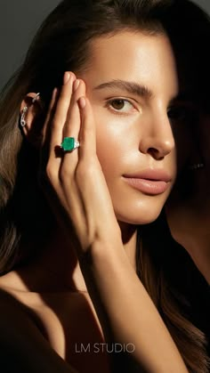 a woman with her hands on her face and wearing an emerald ring, posing for the camera