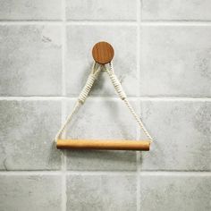 a piece of wood hanging from a rope on a wall with white tiles behind it