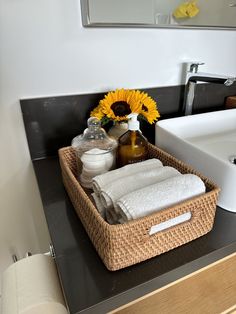 a wicker basket with towels and sunflowers in it on a bathroom counter