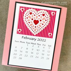 a pink and white calendar with a heart on it's cover, sitting on a table