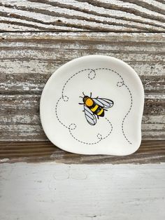 a white plate with a yellow and black bee painted on it's side, sitting on a wooden surface